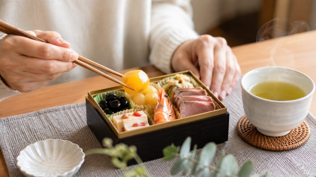 栗きんとんや黒豆などが入ったお試しおせちを箸で試食する様子